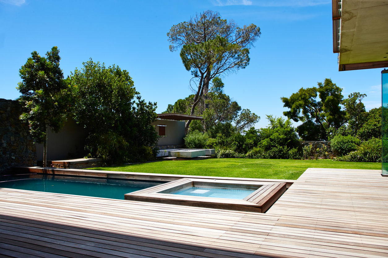 Une terrasse moderne et minimaliste en lattes de bois avec piscine, avec une pelouse et une maison à l'arrière-plan.