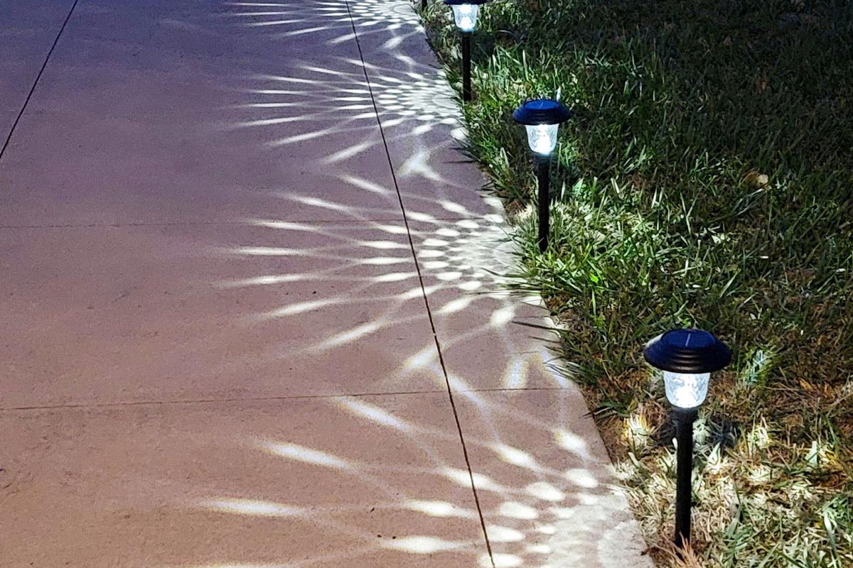 Three black solar path lights casting a decorative patterned glow on walkway at night