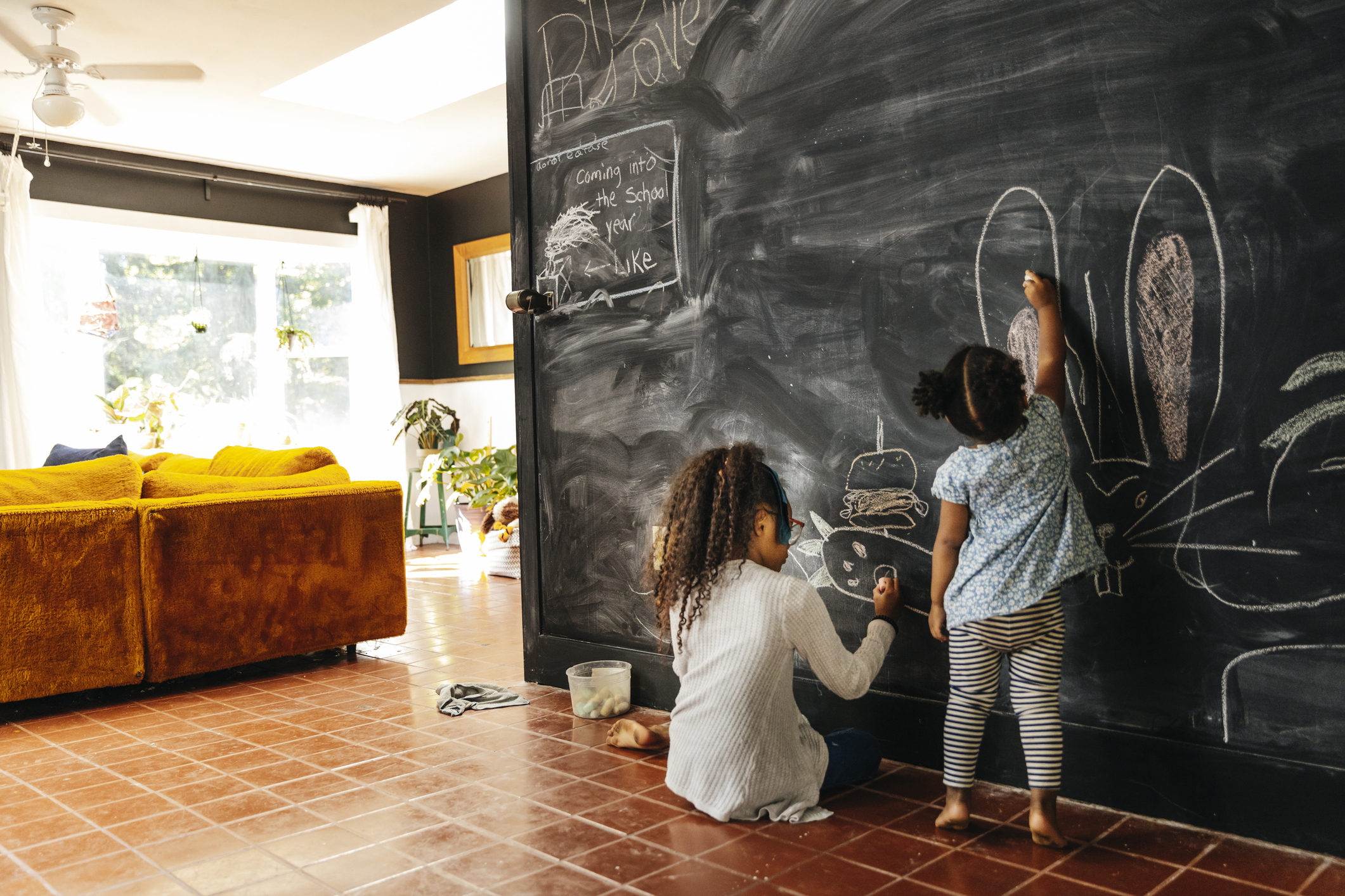 Two children draw on a wall that has been turned into a chalkboard at home