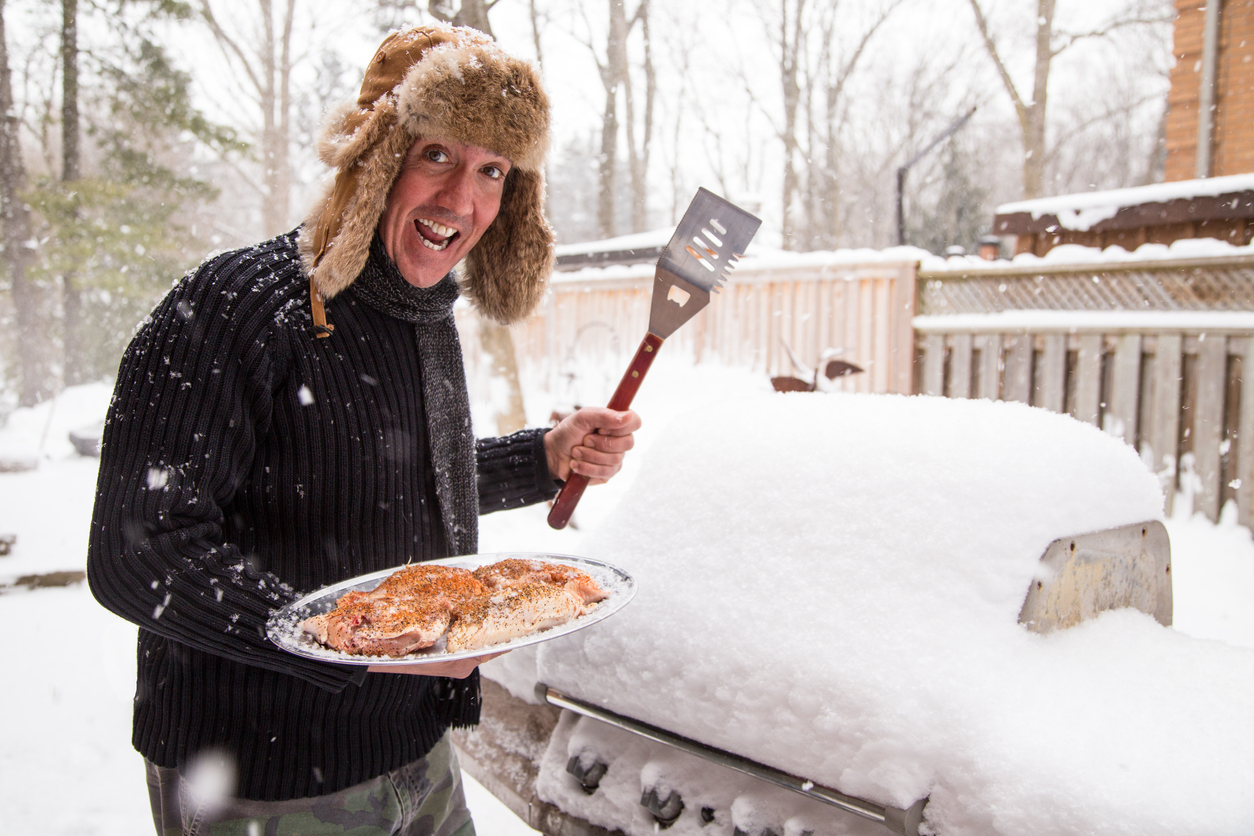 un homme s'approche de son gril avec un plat de poulet. Il est excité à l'idée de faire un barbecue malgré le gros tas de neige gelée