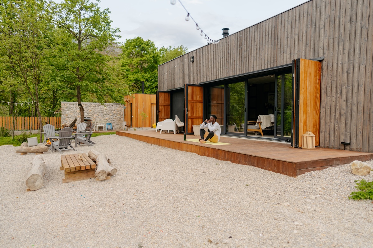 Homme assis sur une terrasse de style moderne donnant sur un patio en gravier avec des meubles de terrasse élégants.