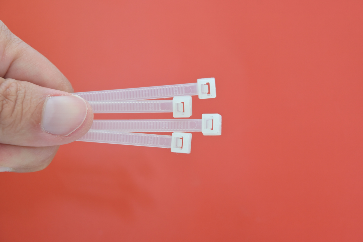 A person is holding a cluster of four undone zip ties in front of a red-orange backdrop.