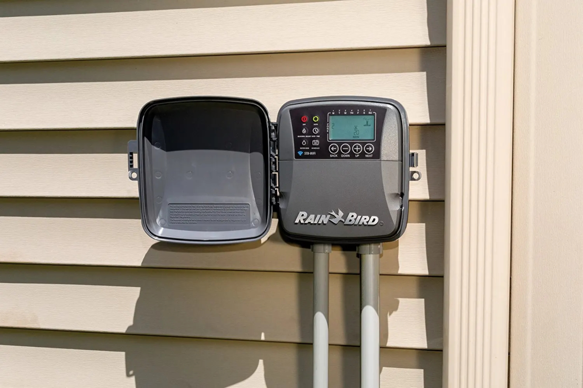 An open Rain Bird Smart Irrigation Controller unit installed on cream house siding.