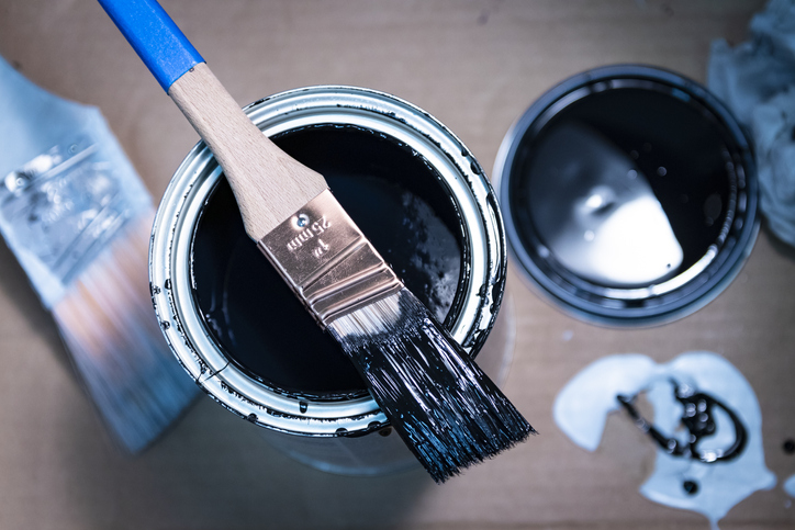 two-paint-cans-with-bllue-paint-inside-under-a-paint-brush-and-on-a-wood-table