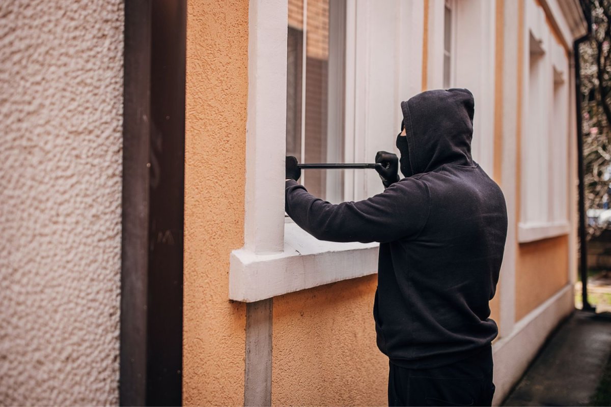 Un cambrioleur habillé en noir utilise un outil pour briser la fenêtre d'un bâtiment.