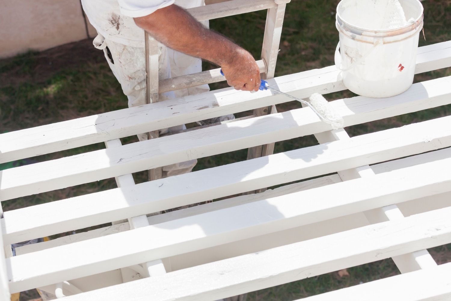 A close-up of a professional using a small paint roller to apply white paint to a wooden deck.