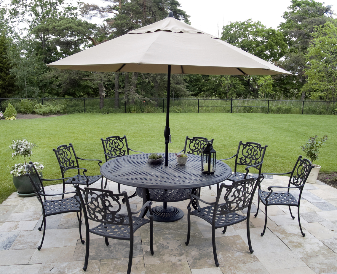 Un parasol de terrasse installé au centre d'un ensemble de patio en métal devant une grande cour herbeuse