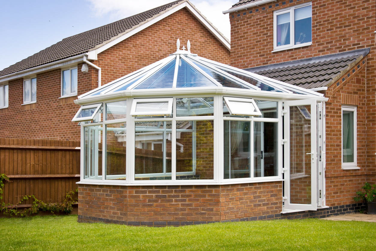 An exterior shot of a glass sunroom built onto the back of a brick home.