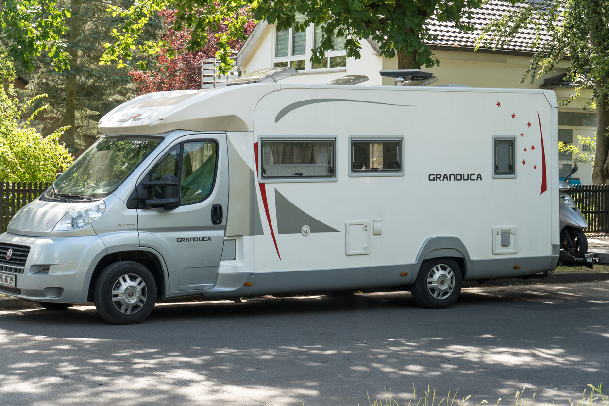 grand camping-car blanc garé dans une rue ombragée dans un quartier résidentiel