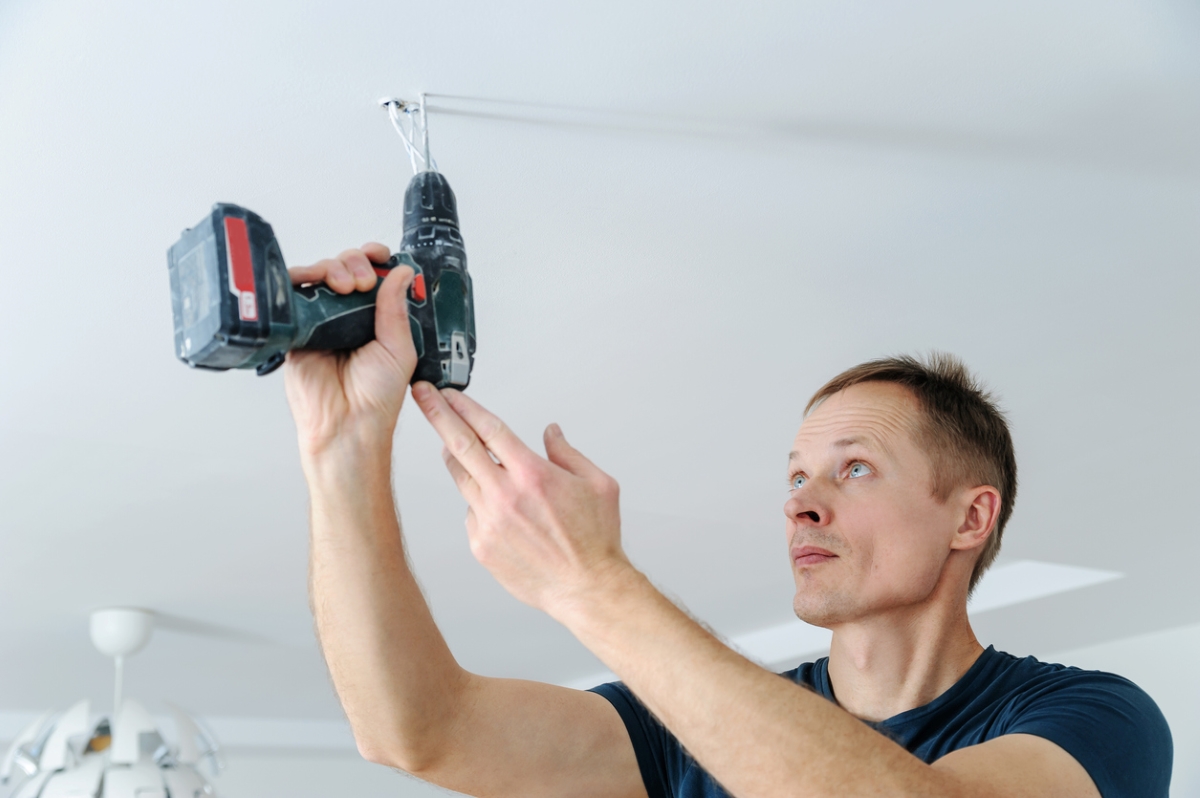 les outils électriques les plus dangereux - un homme perce le plafond avec une perceuse sans fil