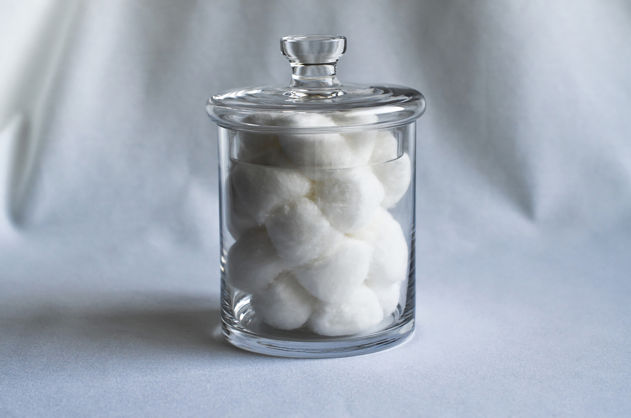 Boules de coton dans un bocal en verre sur une feuille blanche.