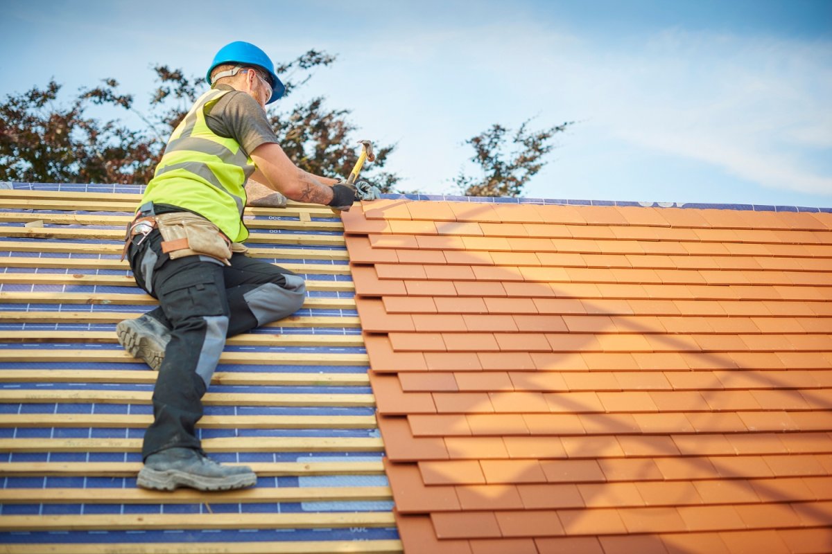 A roofer in a yellow safety vest installs a roof.