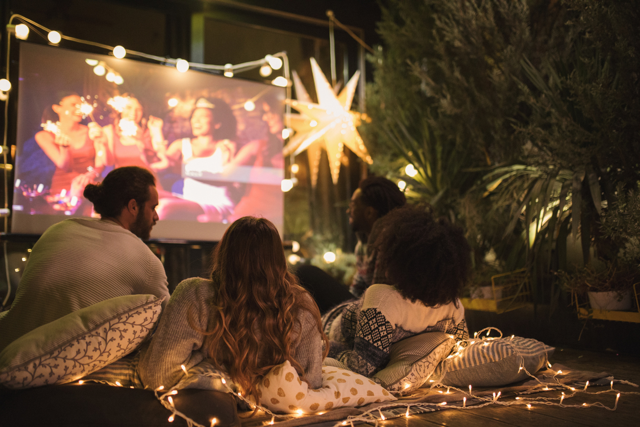 Trois amis regardant un film dans le jardin décoré de guirlandes lumineuses.