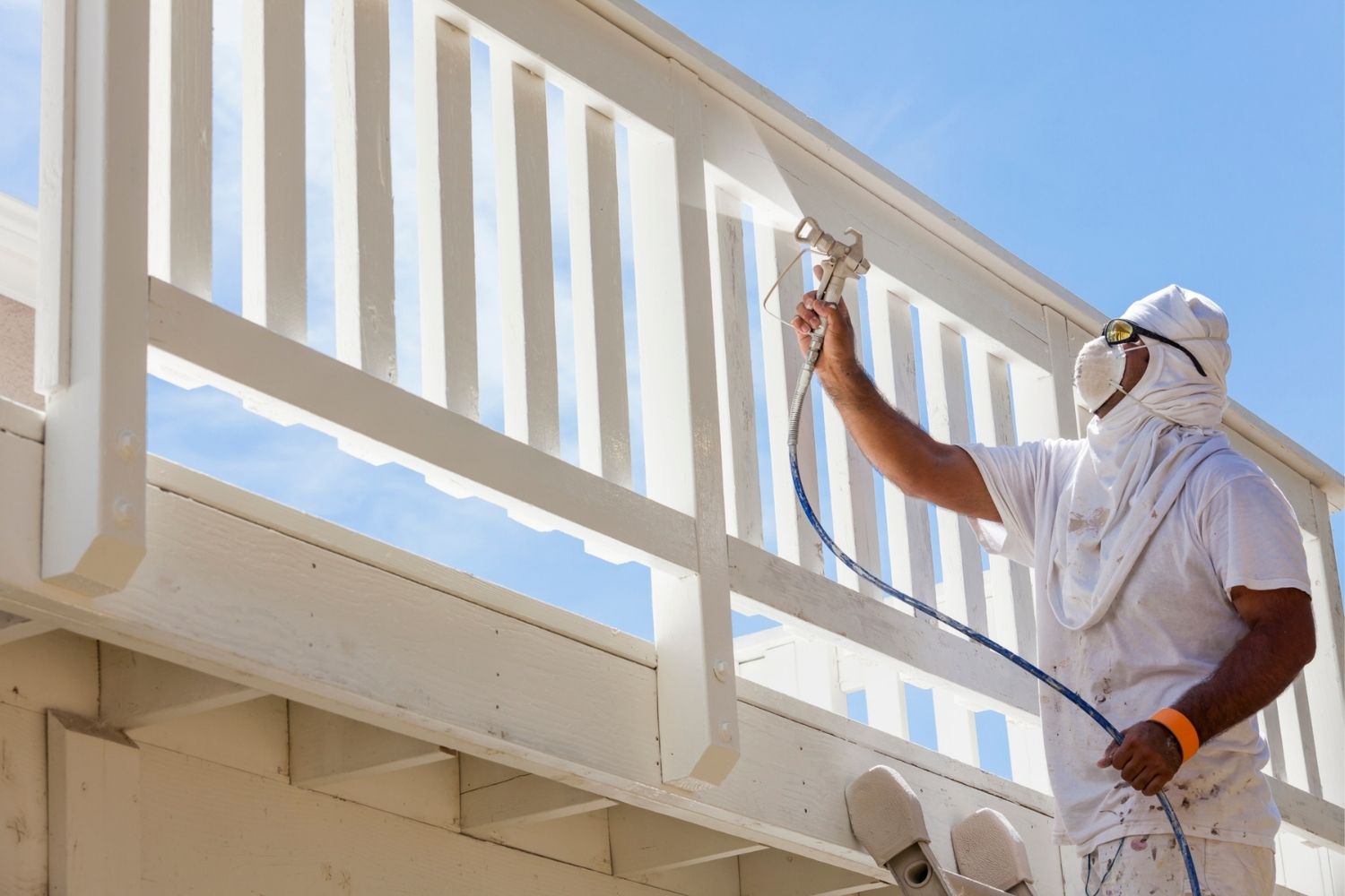 A professional uses a paint sprayer to apply white paint to a wooden deck.