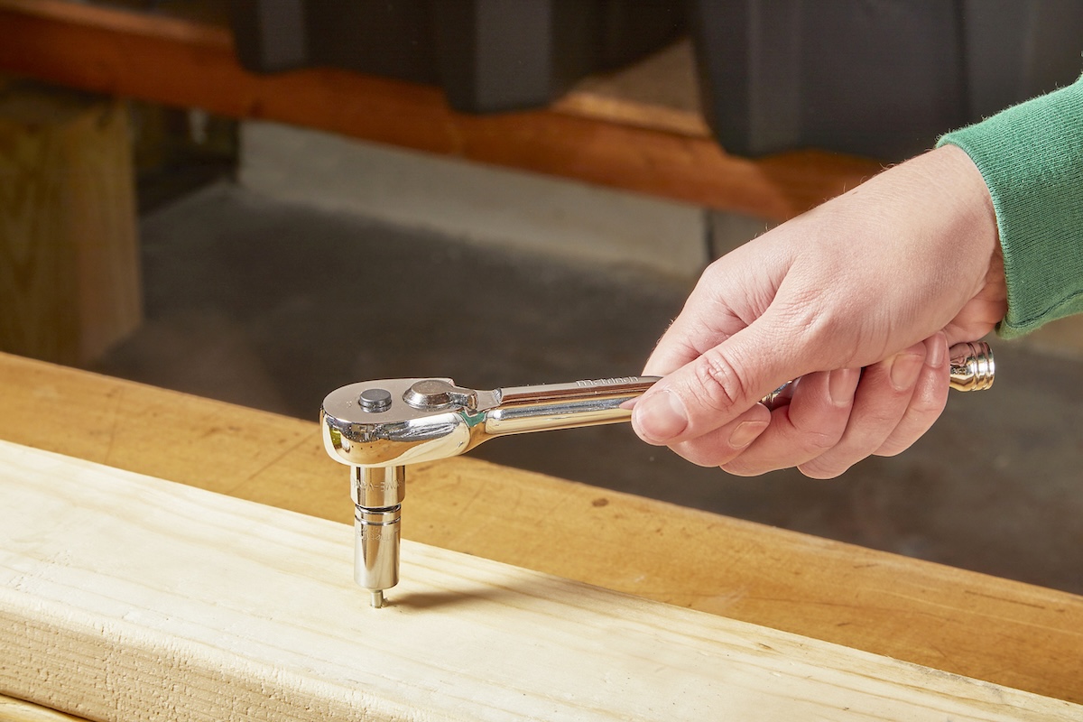 A person using a ratchet wrench to remove a stripped screw with a nut welded onto the head.