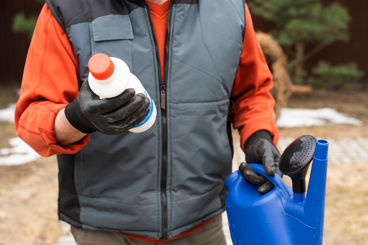 Une bouteille en plastique contenant du désherbant chimique et un arrosoir dans les mains masculines d'un agriculteur