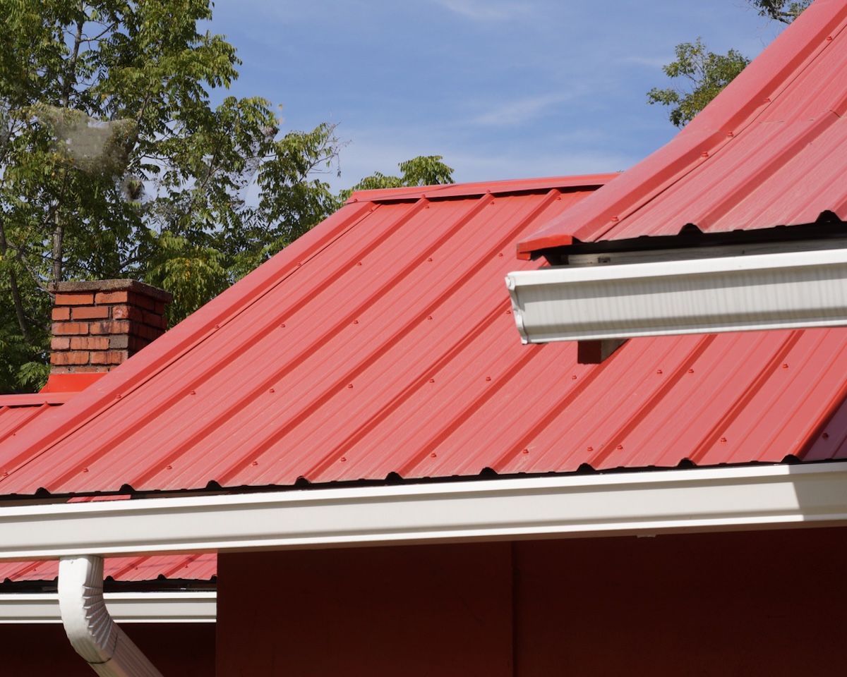 A home with a brick chimney and red metal roof.