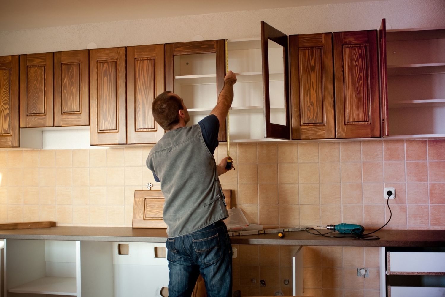 A view of a man measuring wood cabinet doors. 