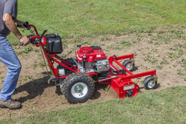 Person using heavy duty red power rake lawn machine.