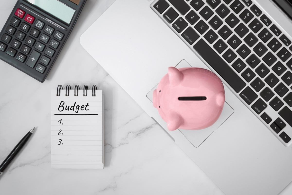 Desk with piggy bank on laptop, notebook, and calculator.