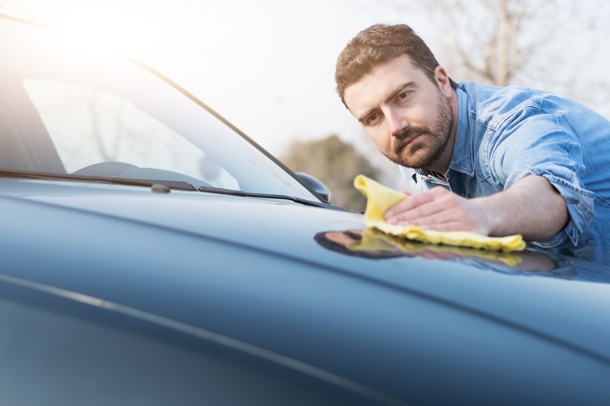 Un homme utilise un chiffon pour nettoyer le capot de sa voiture