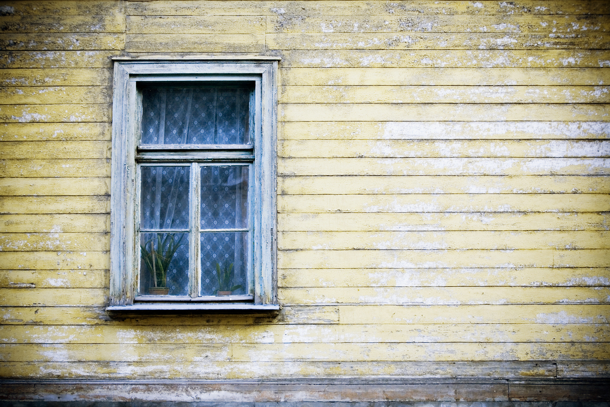 mur extérieur d'une maison avec fenêtre avec rideau de dentelle et revêtement jaune décoloré et écaillé