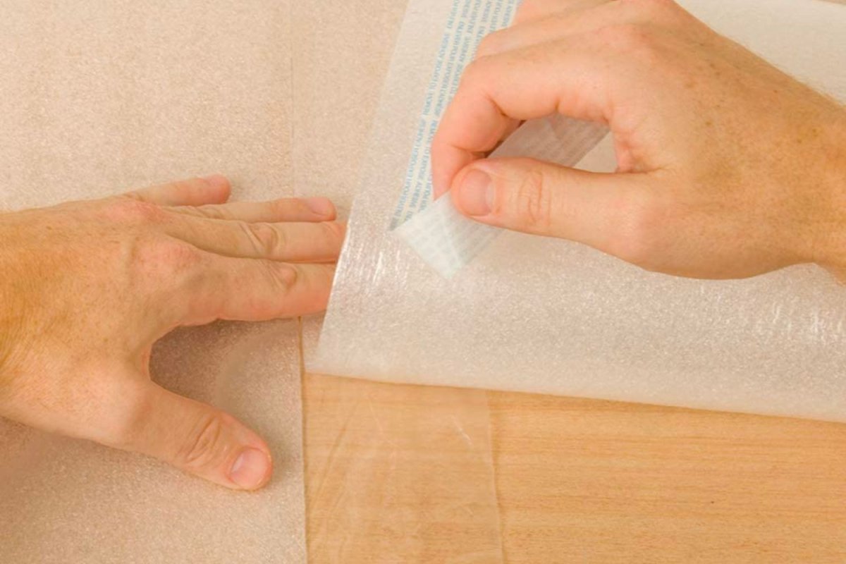 Tearing off adhesive backing strips from flooring underlayment on a wood floor