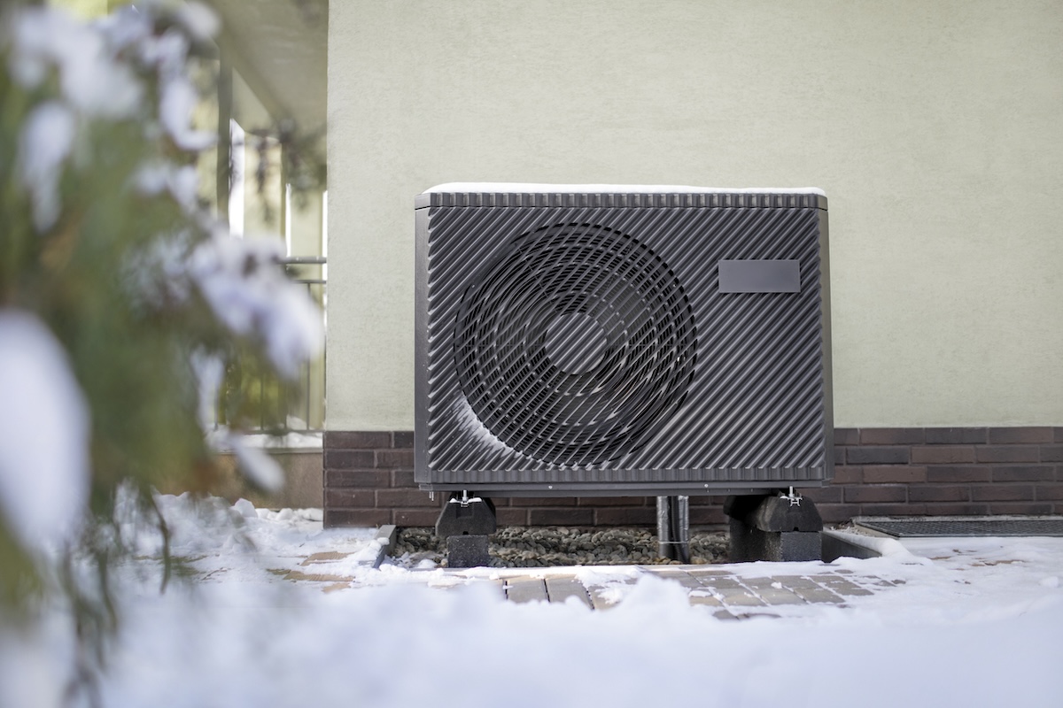 An electric air source heat pump installed outside a home in winter.