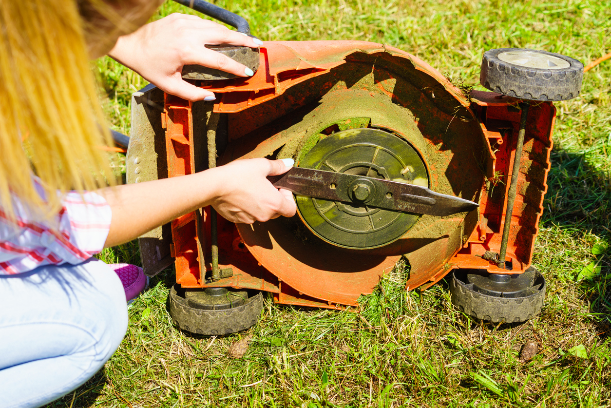 woman crouching to inspect blade of lawnmower