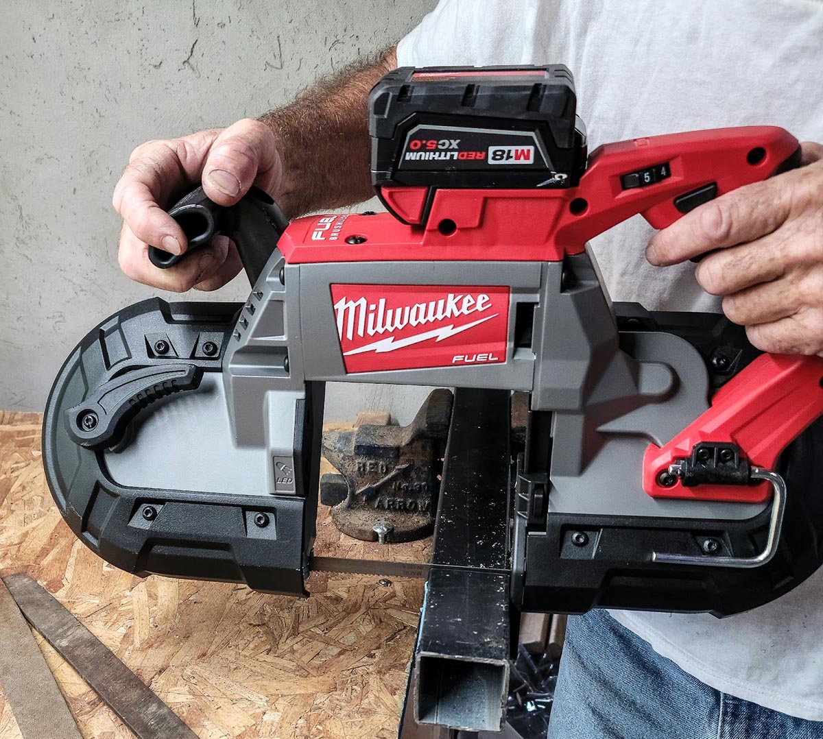 A person holding the Milwaukee 2829-22 M18 Fuel Compact Band Saw over a piece of particle board during testing.