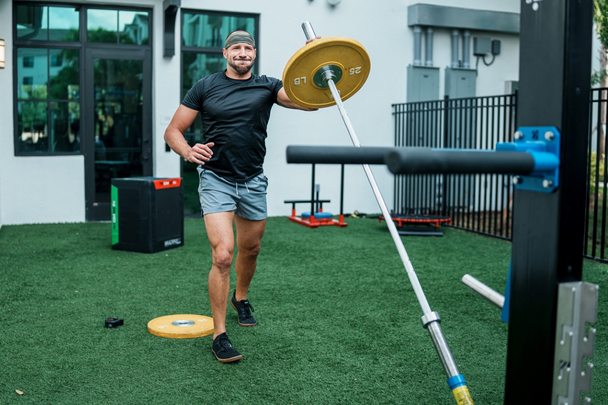 A man lifting large barbell as part of his workout in his yard.