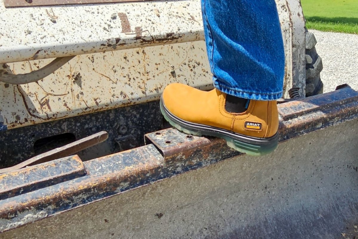 Person in Ariat work boots stepping on the back of a skid steer