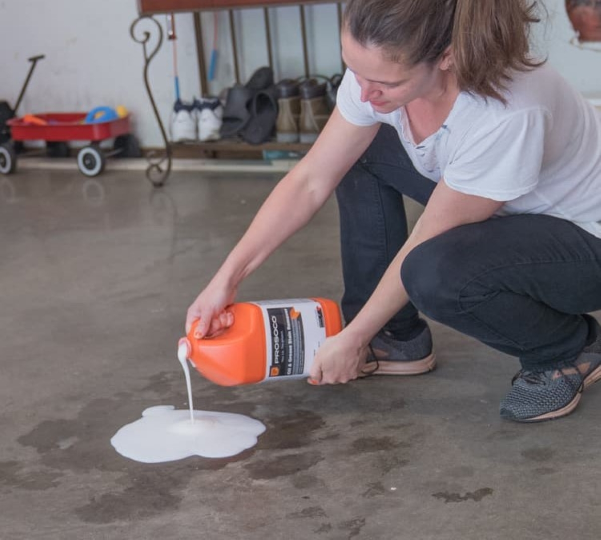 Une femme verse un détachant d'huile et de graisse sur une tache d'essence dans un garage.