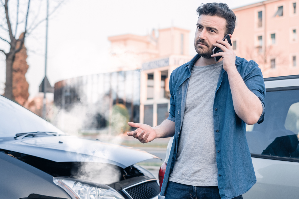 man making a call while smoke is coming out of hood of a car.