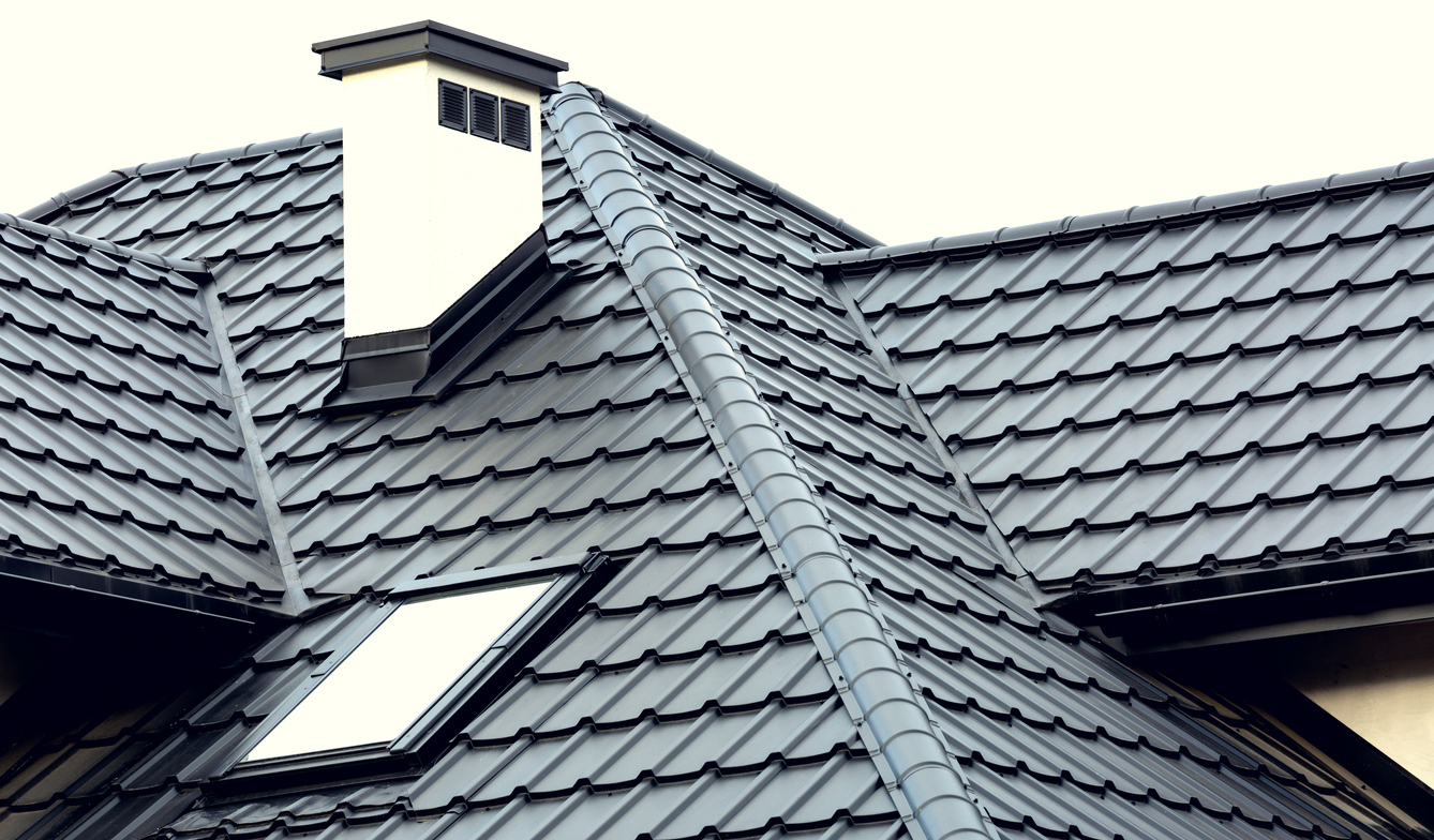 Roof of a new house with slants, a skylight, a plastered chimney and ventilation grilles. Roof covering with steel tiles.