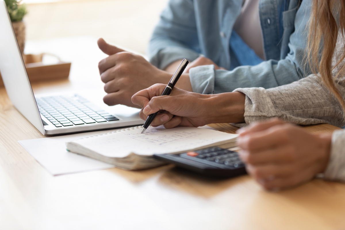 A couple is calculating a budget with a laptop, notebook, and calculator.