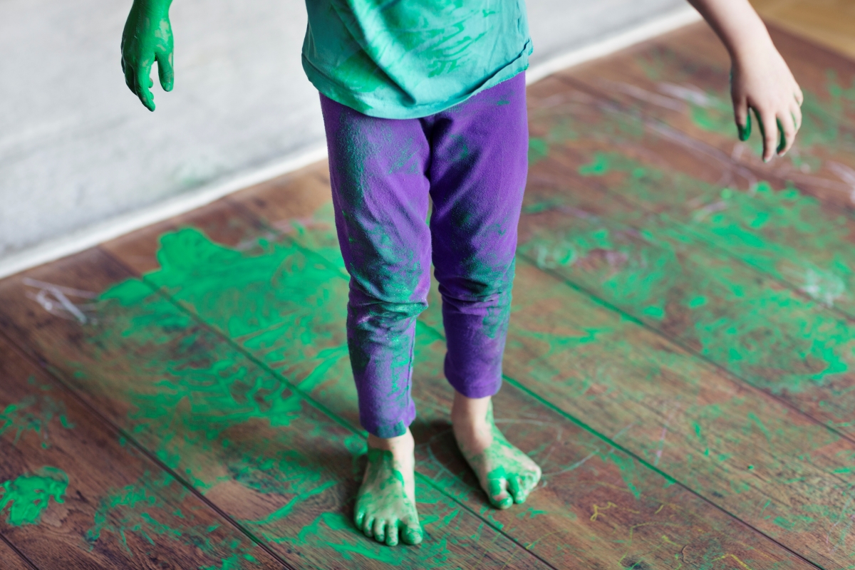 A child and wooden floor is covered in green paint.