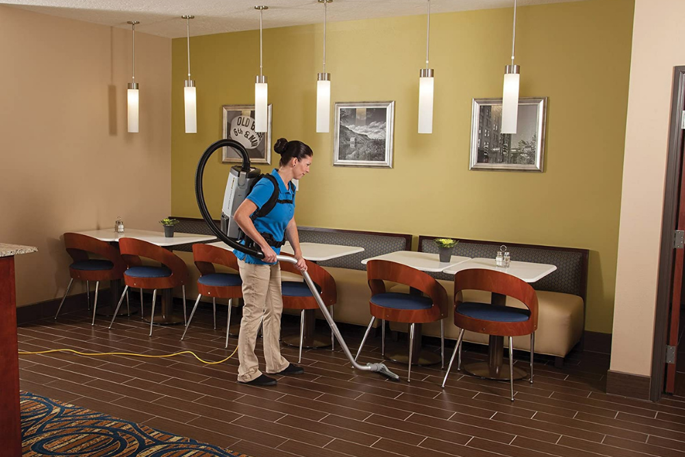 A person using the best backpack vacuum option to vacuum under a table and chairs at a restaurant