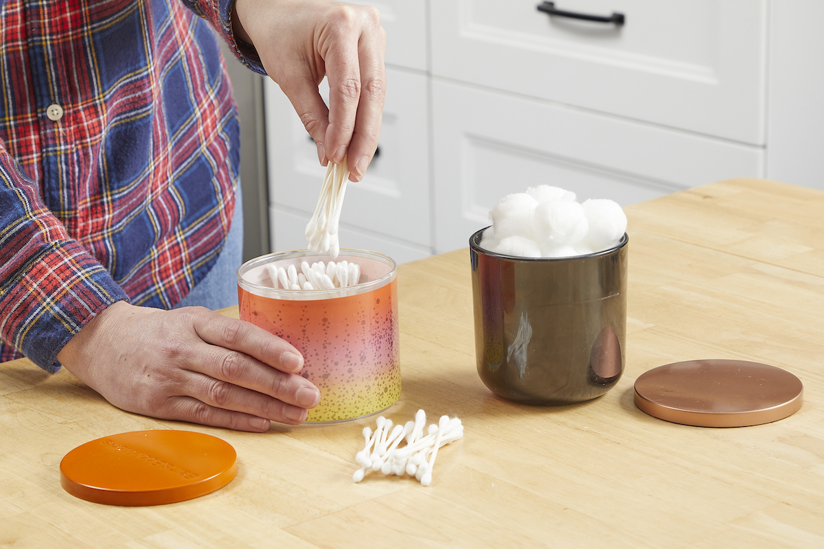 Woman using candle jars to store Q-tips and cotton balls.