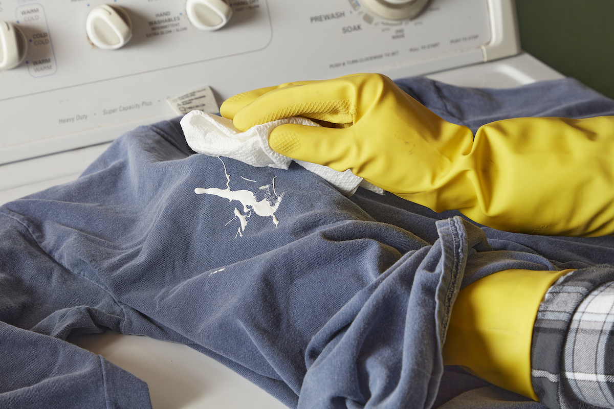 Woman wearing yellow rubber gloves uses a white rag to dab wet paint off a blue shirt.