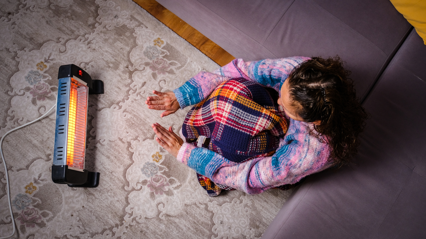 Une personne assise sur le sol se chauffe les mains à la maison sur un radiateur halogène électrique portable