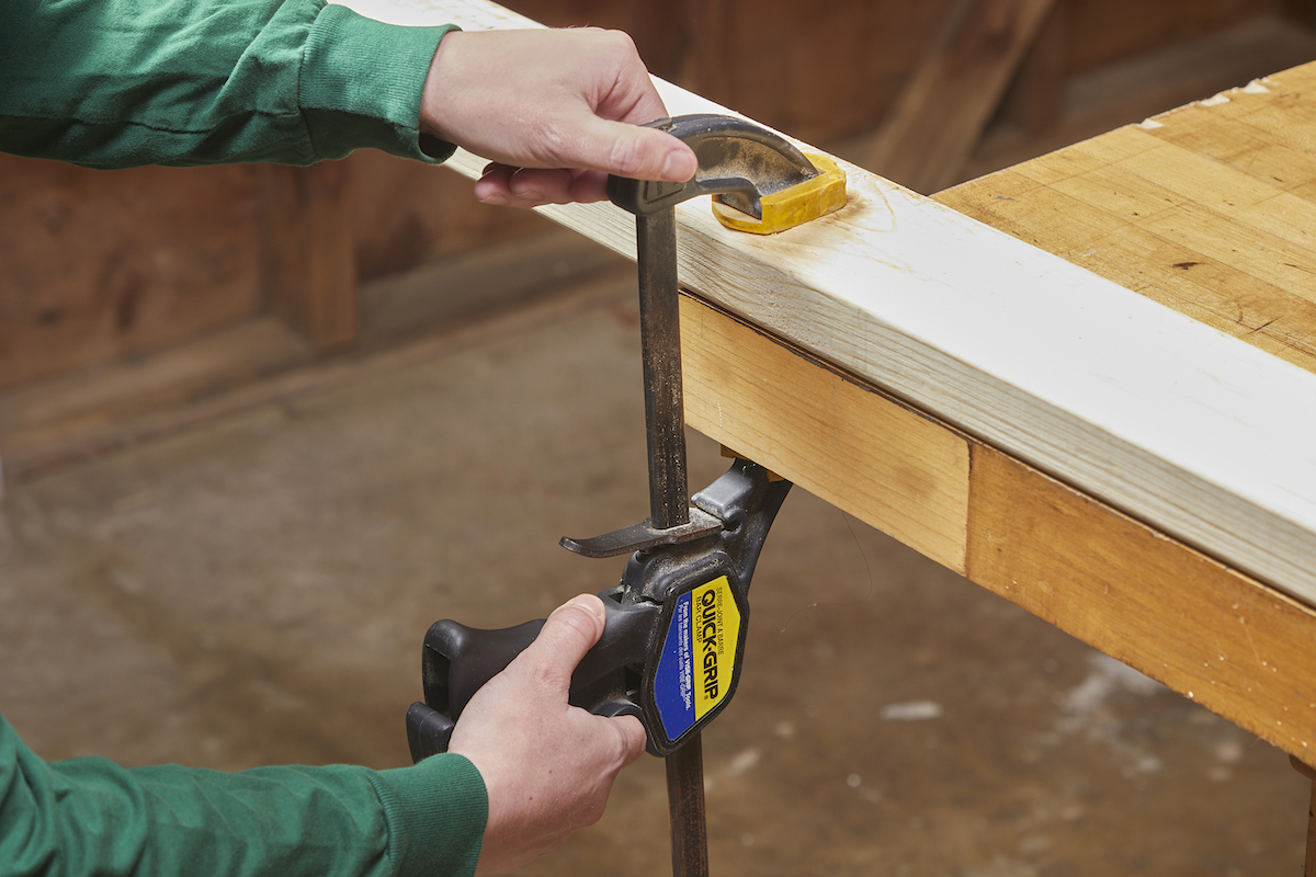 Femme fixant un 2x4 sur une table de travail avant de le couper à l'aide d'une scie circulaire.