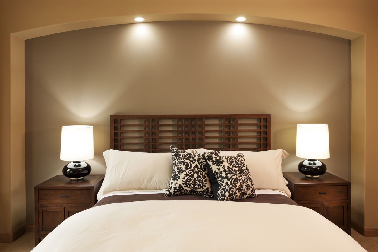 Elegant master bedroom scene in a custom home. Medium stained wood headboard and bedside tables with modern lamps and throw pillows.