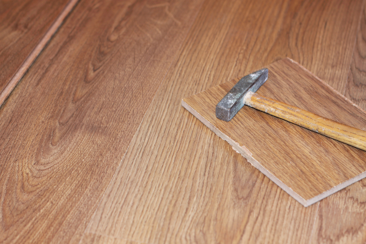 A hammer and a broken faux wood flooring plank rest on top of more laminate flooring.