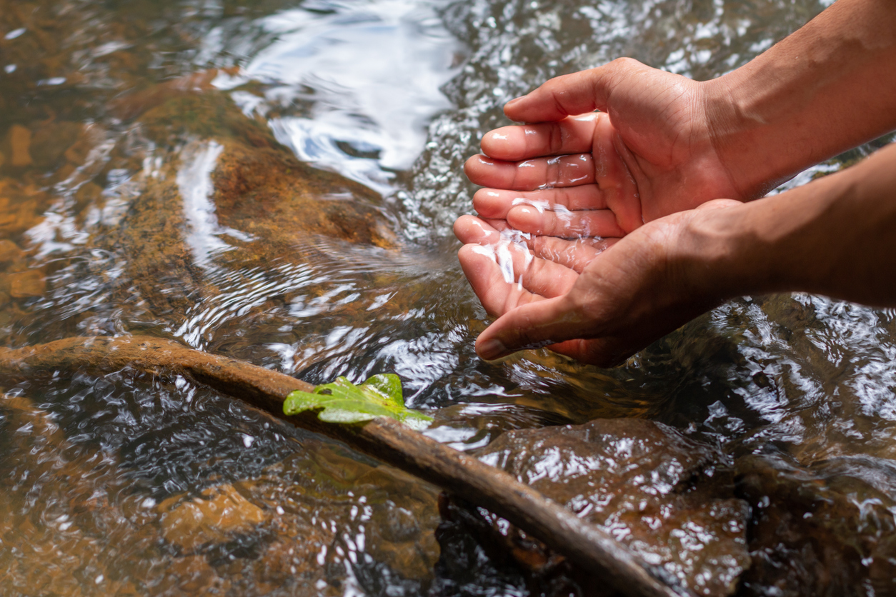 close view of hands drawing water from a fresh water stream