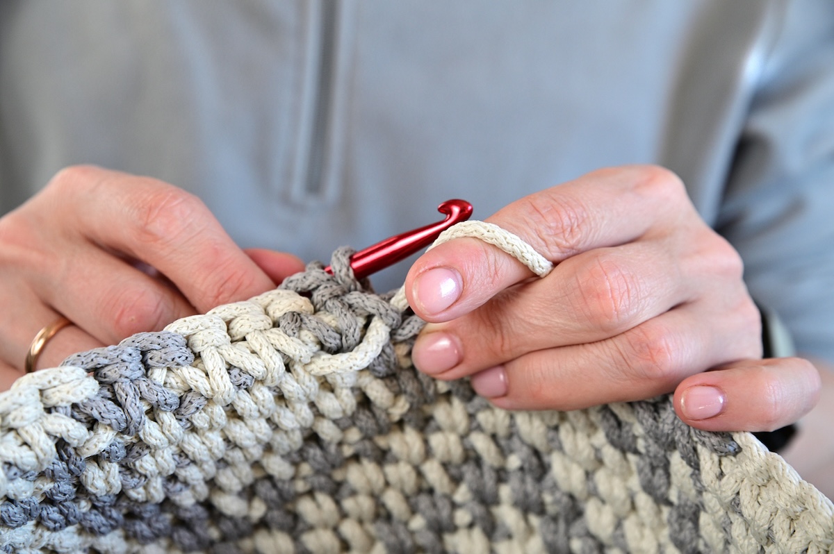 A person crocheting a small basket for decor in their home.