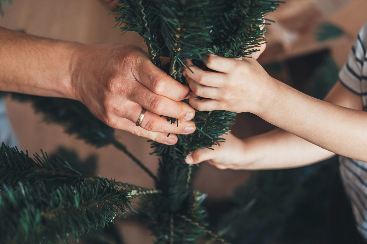 Close-up view of the hands of father and son trying to assemble the artificial Christmas tree together.