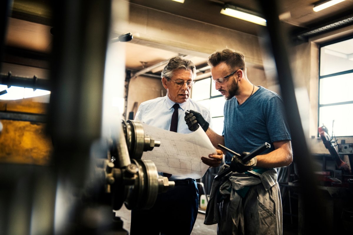 A man in a tie and a welder look at a building plan.