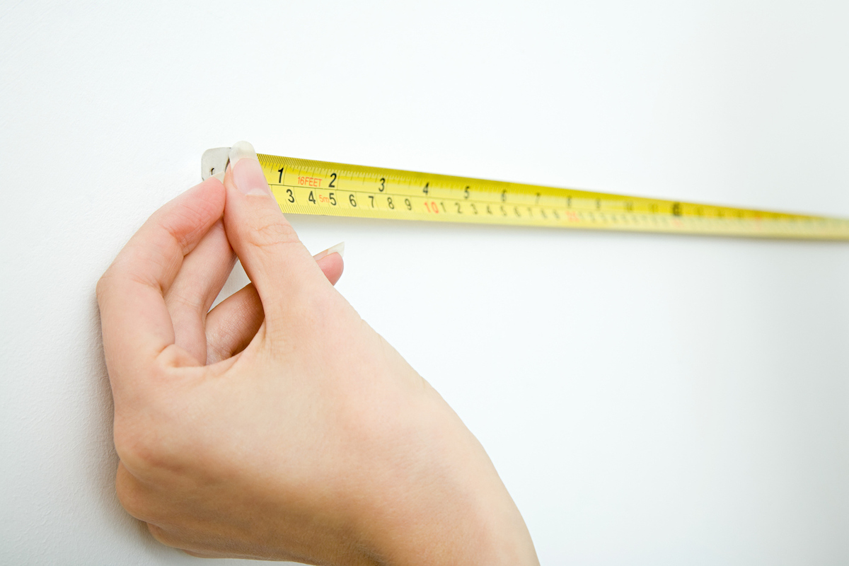 Woman measures a white wall with a yellow measuring tape.