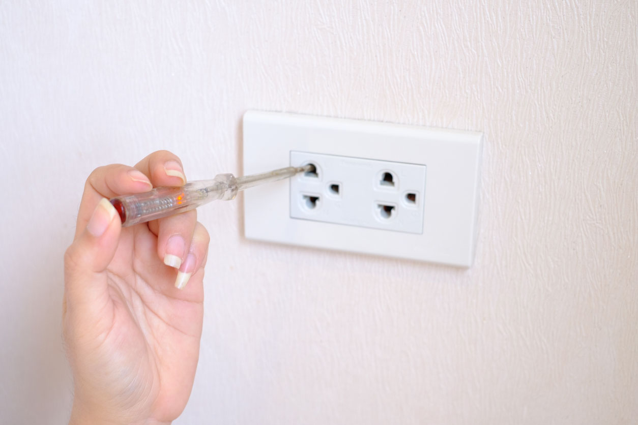 A close up of a hand using a tool to fix an outlet.